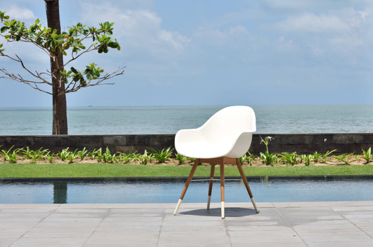 A white resin chair with wooden legs placed beside a pool with a view of the ocean.