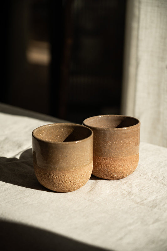 Rustic pinkish red stoneware cups set on a white cloth.