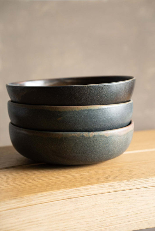 Stack of rustic stoneware bowls with a subtle earthy glaze on a wooden surface