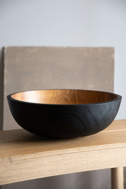 Large wooden bowl, dark outer finish, lighter inner finish, displayed on wooden shelf, neutral backdrop