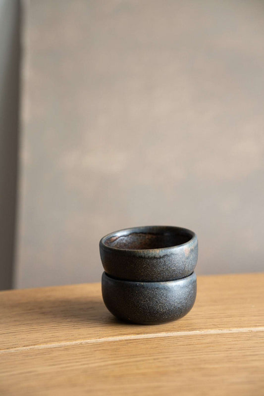 Stack of dark, rustic, metallic pinch bowls. Wooden table backdrop.