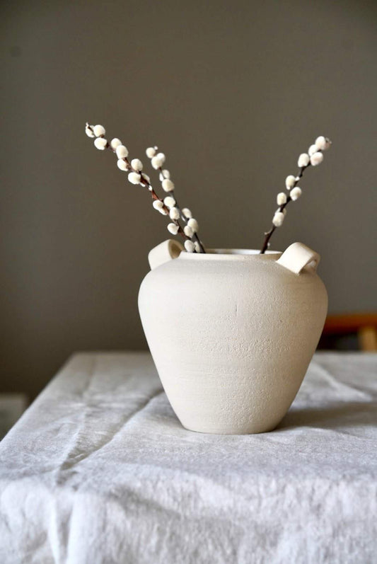 Textured white stoneware vase with two branches of white berries. Background is plain