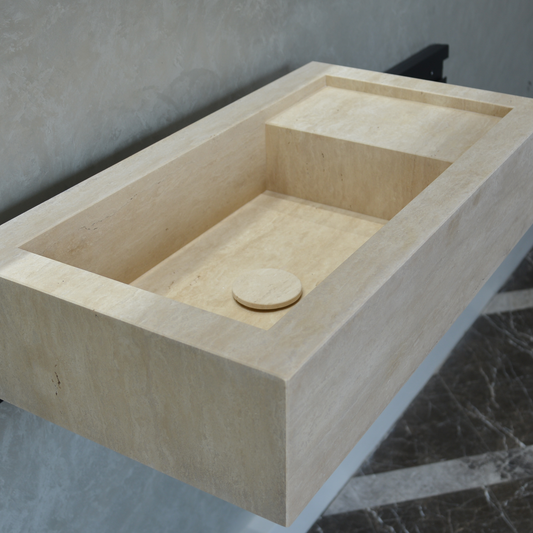 Handmade travertine bathroom sink in light beige tones, sitting on a marbled surface.