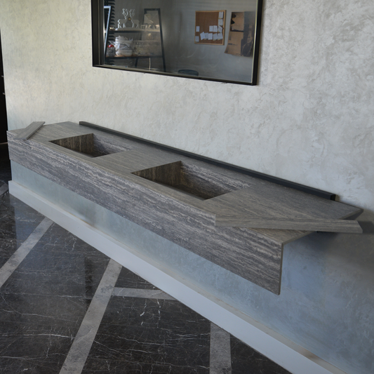 Engineered stone sink in Travertino Grey with a deep, contemporary design, displayed in a showroom setting with textured walls and polished marble flooring.