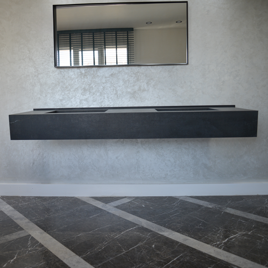 Floating black marble sink with rectangular basins, set against a textured wall with a mirror above.