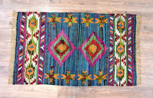 A handmade rug with a vibrant geometric pattern and multi-colored stripes on a wooden floor.