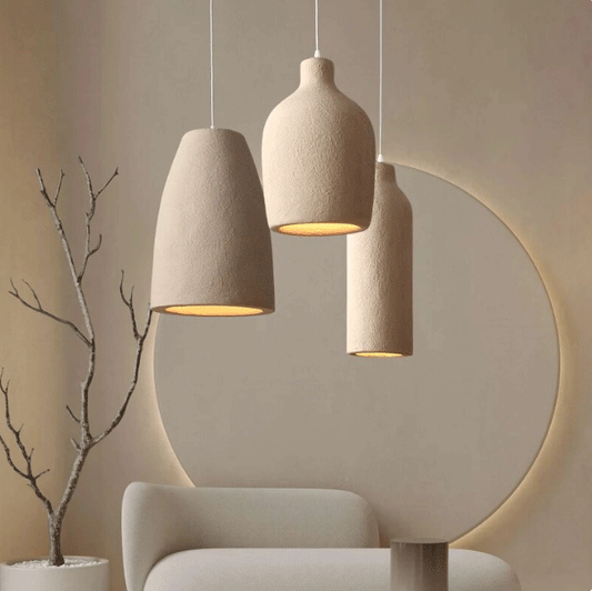 Minimalist ceramic pendant lights with a textured finish lighting up in a modern indoor setting featuring a couch and a tree-like branch in a minimalist styled room.