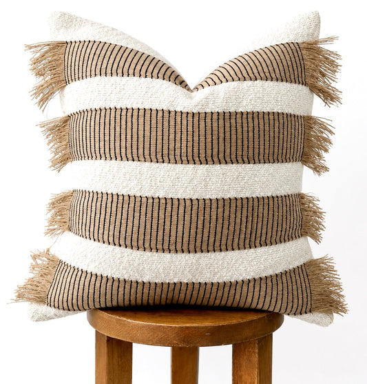 Off-white pillow covers with brown stripe and tassels, stacked on wooden stool.