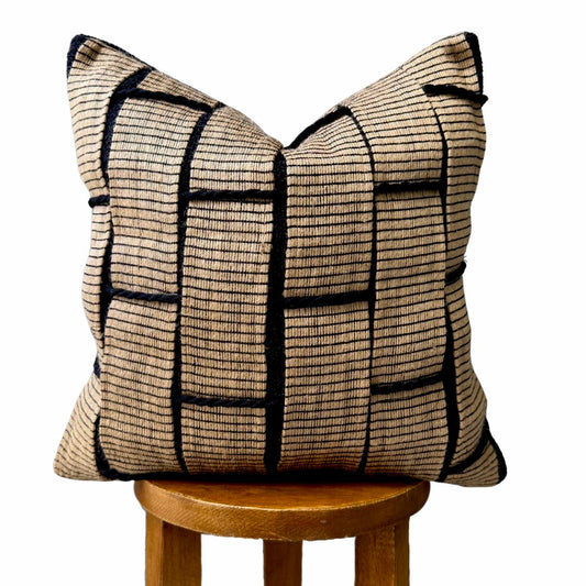 Beige and black textured pillow with grid pattern, displayed on a wooden stool.