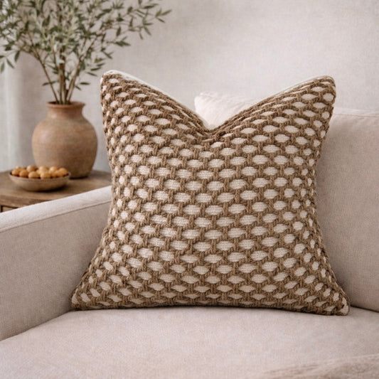 Crochet-patterned pillow cover in beige and cream, placed on a beige sofa, with a plant and bowl in the background