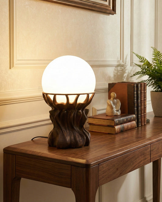Handcrafted solid wood table lamp with frosted glass shade on wooden table. Surrounding books and sculpture.