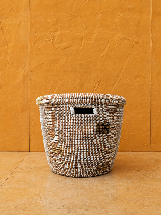 Minimalist white round basket with gray squares on earthy orange wall, light brown woven texture, no visible text or logos