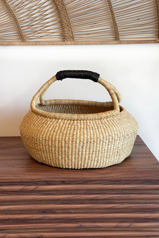 Rattan basket with woven lid and leather handle on wooden table