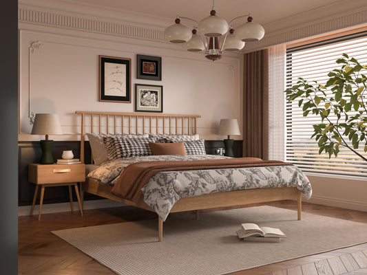 A wooden bed frame with a patterned quilt, next to two side tables with lamps, a chandelier, and framed artwork.
