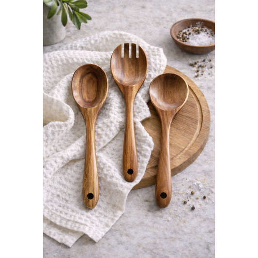 Three wooden salad serving utensils of varying shapes and sizes, placed on a white textured cloth and wooden surface.