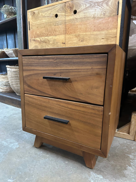 A wooden nightstand with dark metallic handles and visible wood grain, placed on a concrete floor in a store.