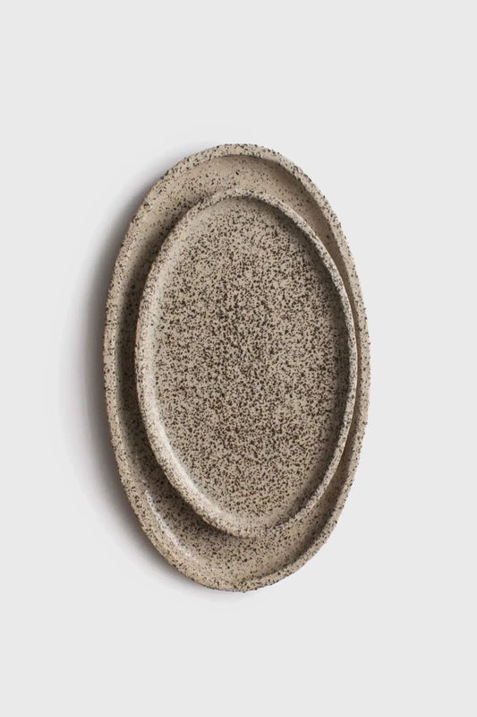 Two large, oval-shaped serving platters made of stoneware with a textured, speckled surface, stacked on top of each other against a white background.