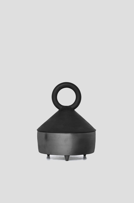 A tall, matte black serving bowl with a lid featuring a ring handle and a metallic base against a plain background.