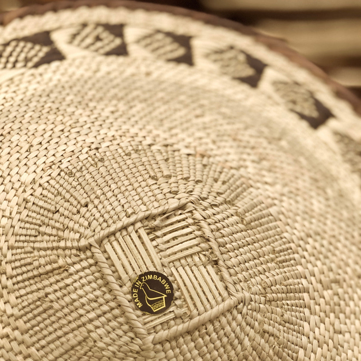 Close-up of a naturally woven Tonga Basket with geometric patterns and a 'Made in Zimbabwe' label.