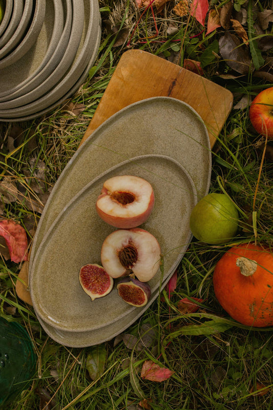 Olive green stoneware serving platters on grass with fruits.