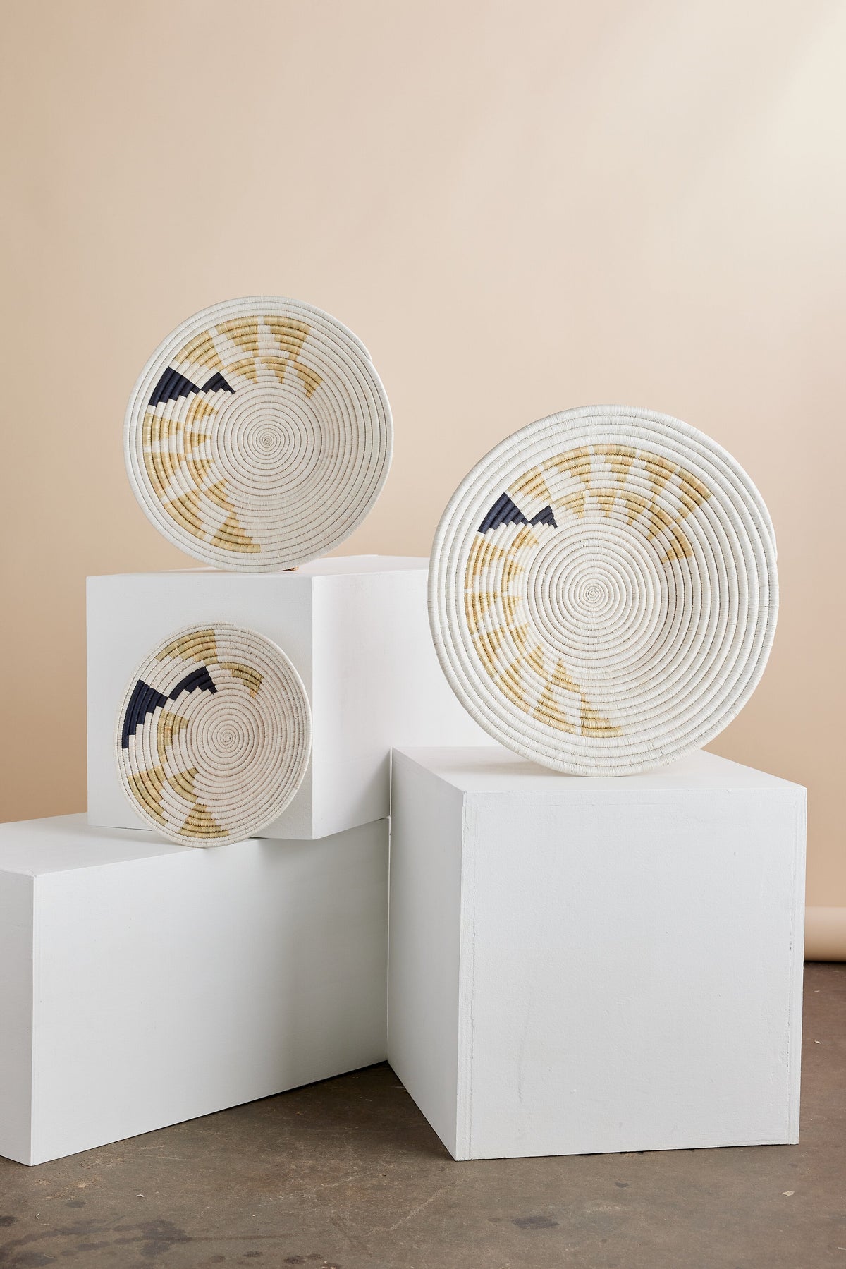 Three Inyabu Wall Baskets with beige, white, and dark tones on white cubes against a plain background