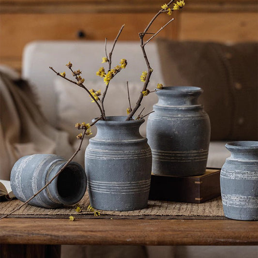Gray clay pottery vase with a simple floral arrangement on a wooden shelf.