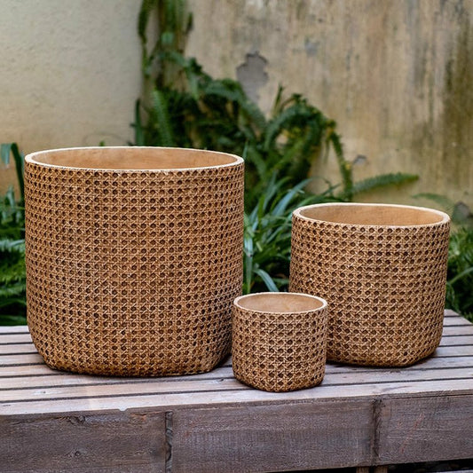 Three wicker texture cement planters in different sizes on a wooden surface with greenery in the background.
