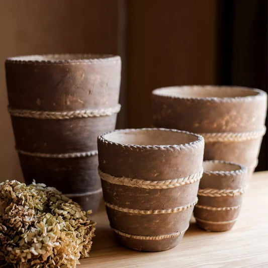 Rustic terracotta planters with rope ties, various sizes, arranged on a wooden surface.