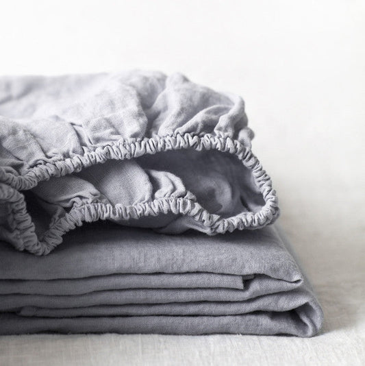Stacked light grey linen fitted sheets with subtle texture