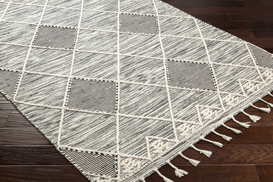 A grey and white woven rug with tassels on a hardwood floor.