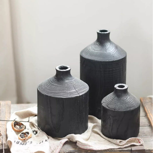Set of black wooden vases with textured finish placed on a rustic surface with fabric and dried flowers