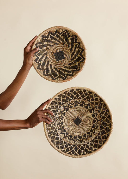 Circular woven baskets with abstract patterns held up against a plain background