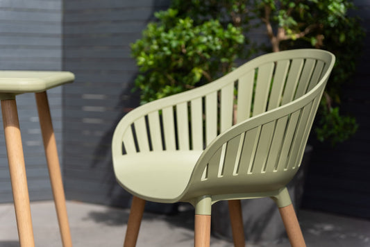 Sage green armchair with slatted back, natural wooden legs, outdoors.