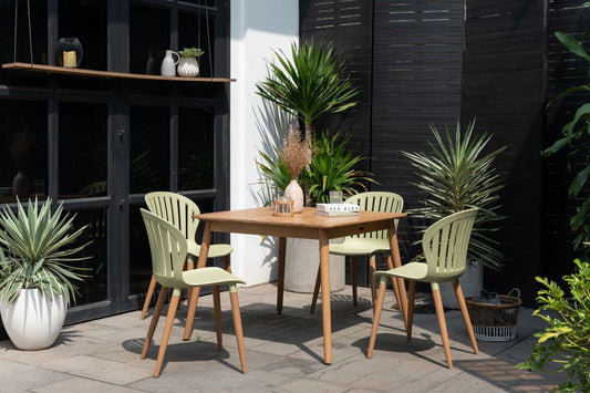 Nassau Square Hardwood Table with four green chairs, set in a patio with plants and black lattice in the background.
