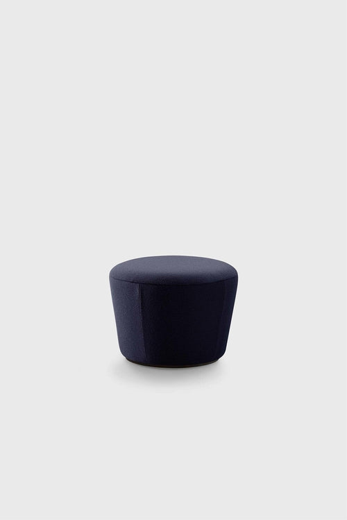 A navy textured pouf with a rounded shape and thick fabric in a minimalist setting.