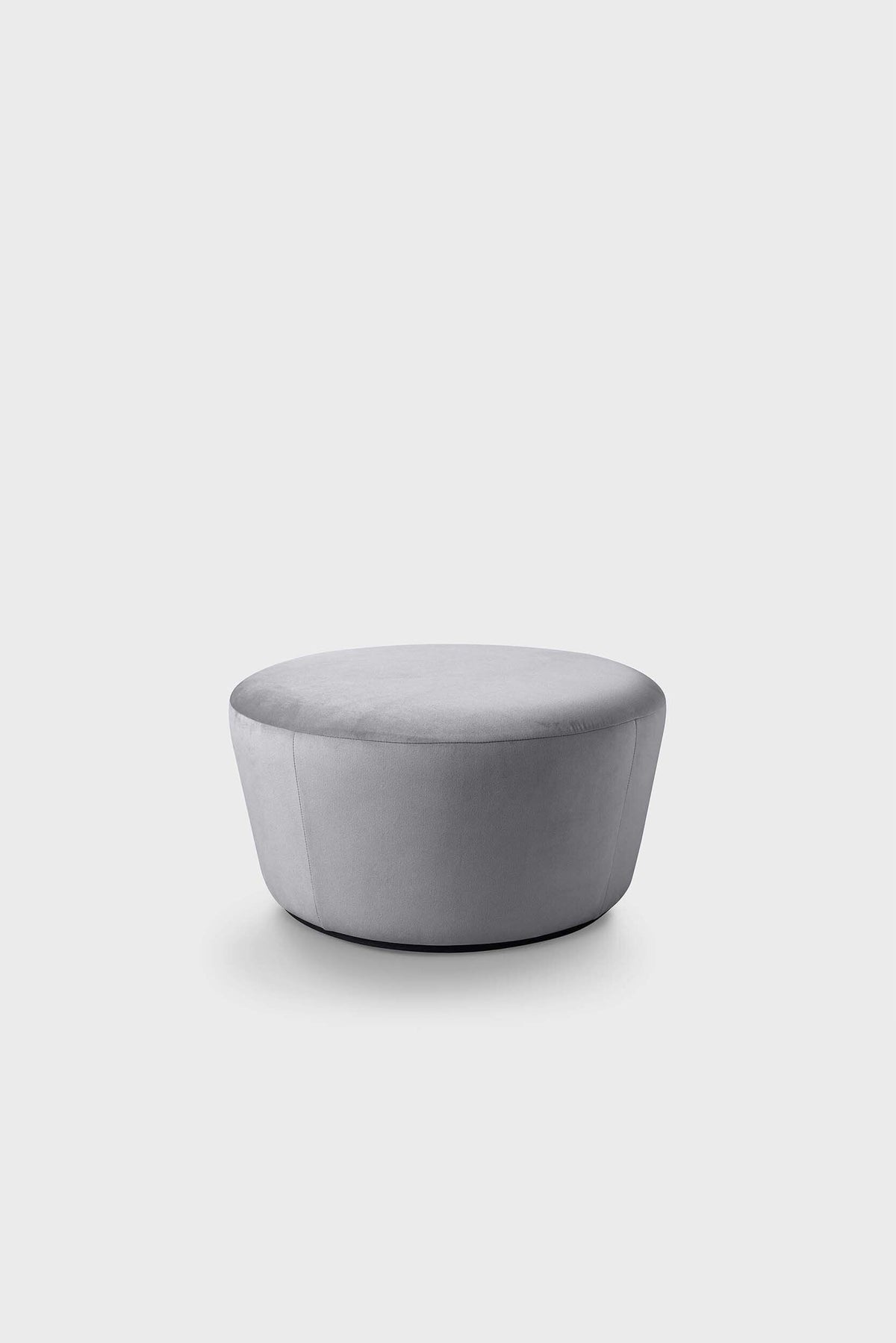 A round, light gray pouf with a velvety texture, placed on a plain white surface.