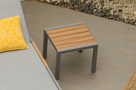 A small square side table with teak top and dark gray legs, placed on a tiled outdoor patio
