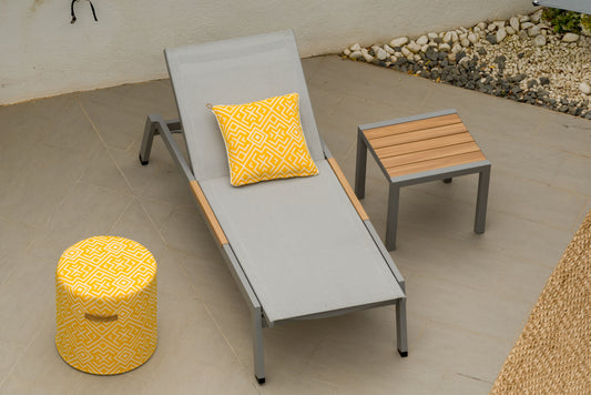 A Panama Light Sun Lounger with a grey frame and orange accents, accompanied by a small end table and matching cushion, set outdoors on a tiled patio with a pebble garden in the background.