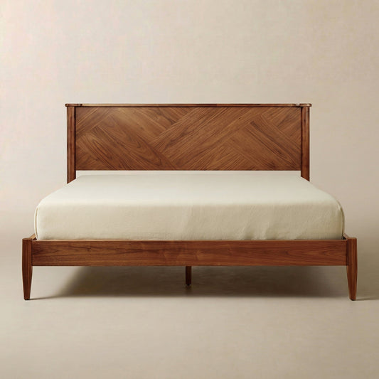 A solid wood bed frame with a geometric headboard in a warm, polished tone, neatly set up in a minimalist room.