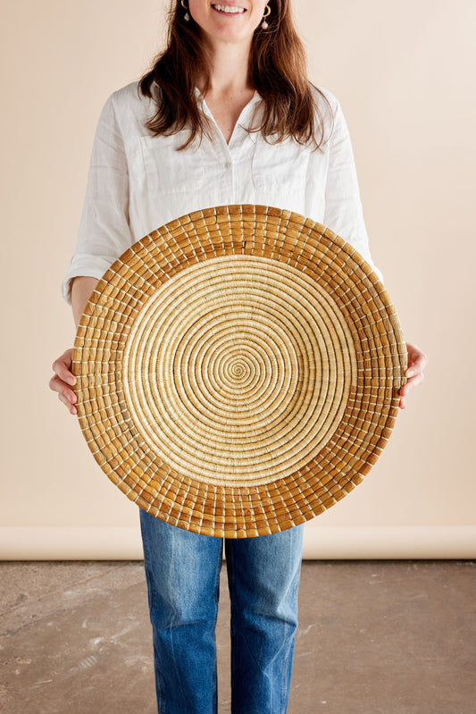 Circular woven basket held by a person in a light, natural setting.