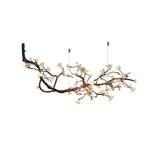 An organic wood branch chandelier decorated with cream flowers and small lights, set against a white background.