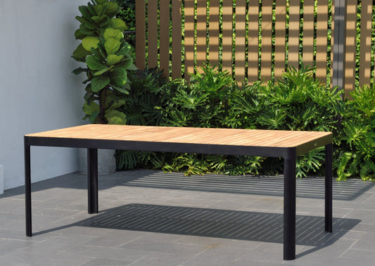 Dark rectangular dining table with wood top and metal legs in a garden setting.
