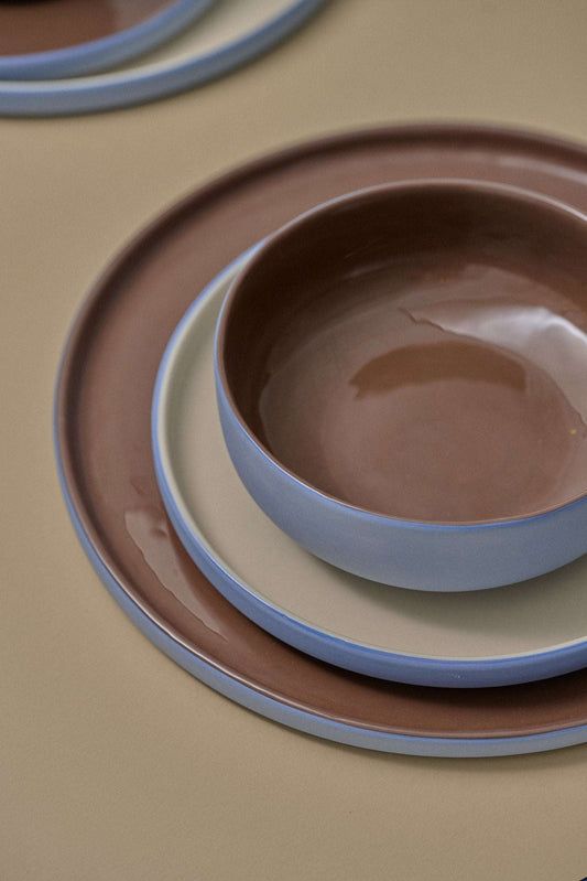 Handmade porcelain bowl in forget-me-not and chocolate colors, stacked on a plate, on a beige surface.