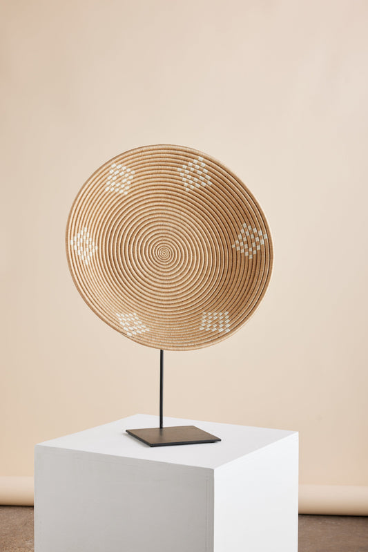 Circular wall basket with a spiral pattern and small white decorative motifs on a cream-colored background, displayed on a white pedestal.