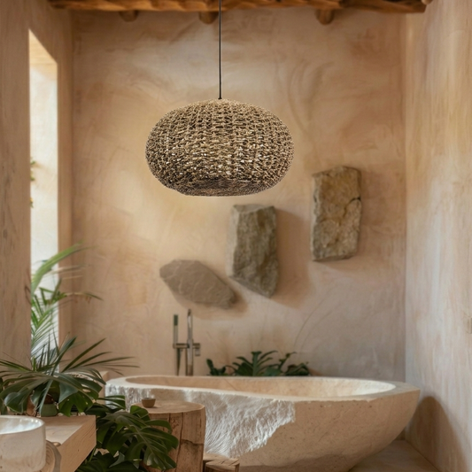 Handwoven jute pendant light hanging above a stone bathtub, surrounded by plants and rough stone panels on the wall.