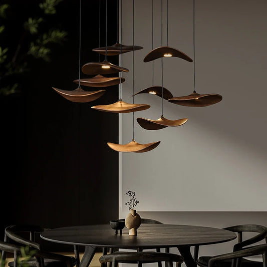 Glowing wooden pendant lights suspending over a round table in a modern dining space, dark table and chairs, wall decor visible.