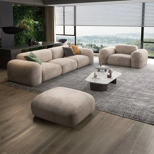 Beige plush sectional sofa with ottoman, dark marble top coffee table, grey rug, minimalist decor.