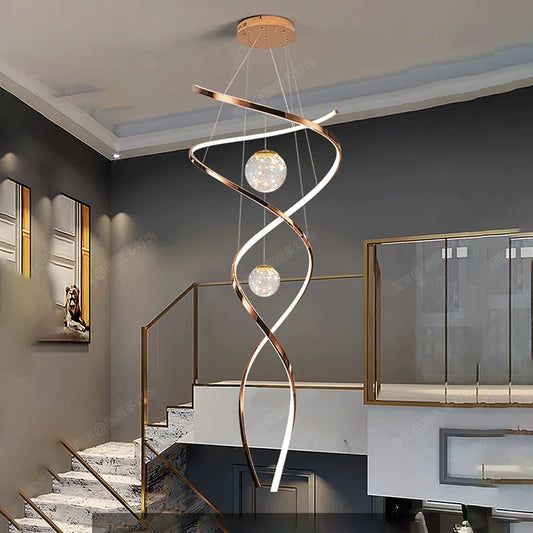 A modern spiral chandelier with two glass balls, hanging from a ceiling in a stairwell with white steps and brass railings.