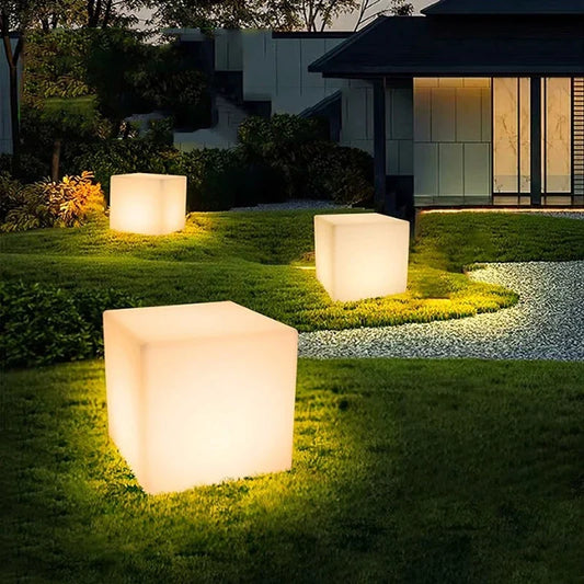 Three white cube-shaped lights on grass with a house in the background