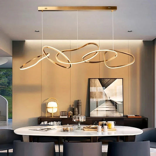 Modern rings pendant lights in black and gold hanging over a dining room table with gray chairs, white tabletop, and abstract wall art.